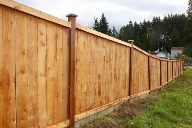 Cedar-toned wood privacy fence with posts and horizontal rails running along a grassy property line