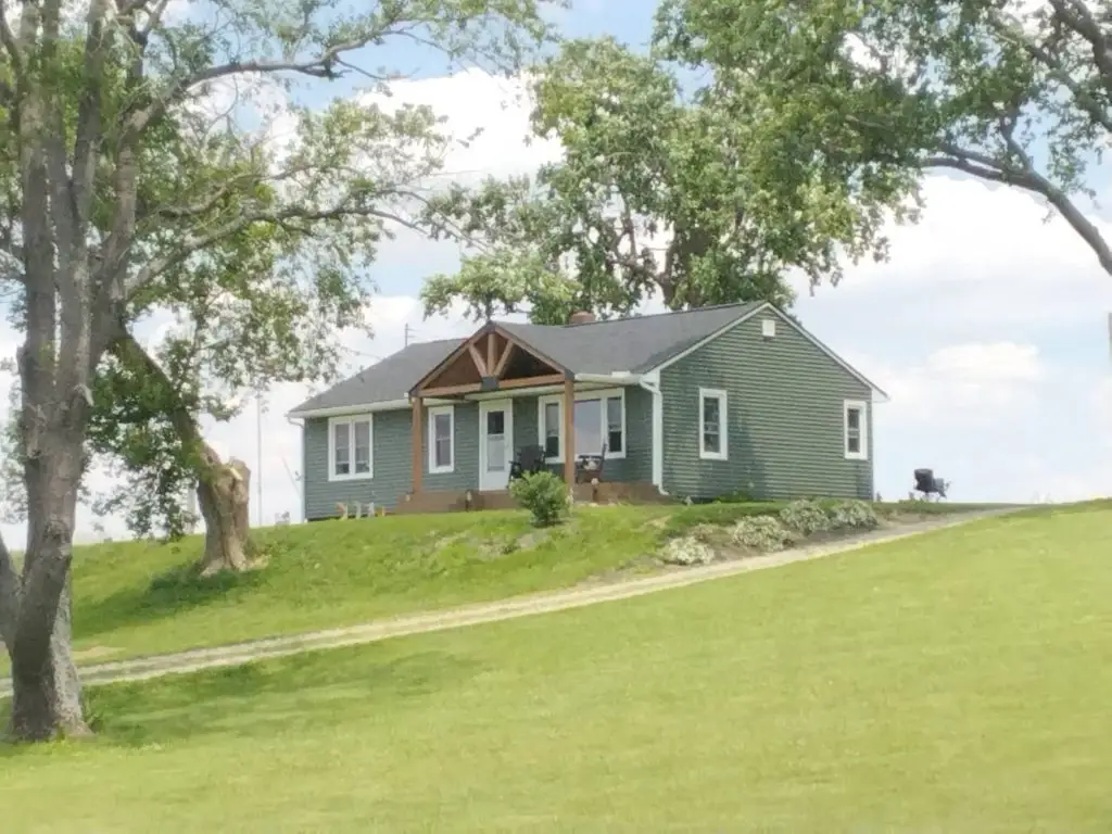 Completed green lap siding replacement with white trim on a Central Ohio farmhouse, viewed from the driveway