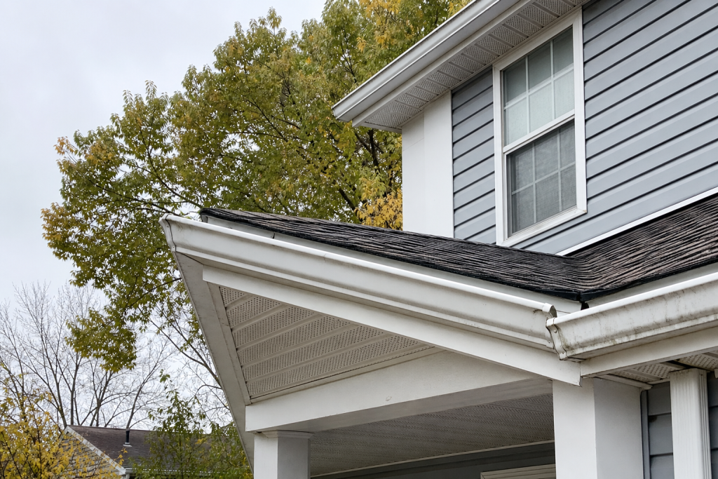 Close view of a soffit and fascia repair area on a Central Ohio home, showing white vented soffit panels, fascia board, and gutter along the eave · AI-generated illustrative photo